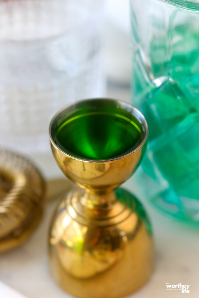 green alcohol in a gold jigger
