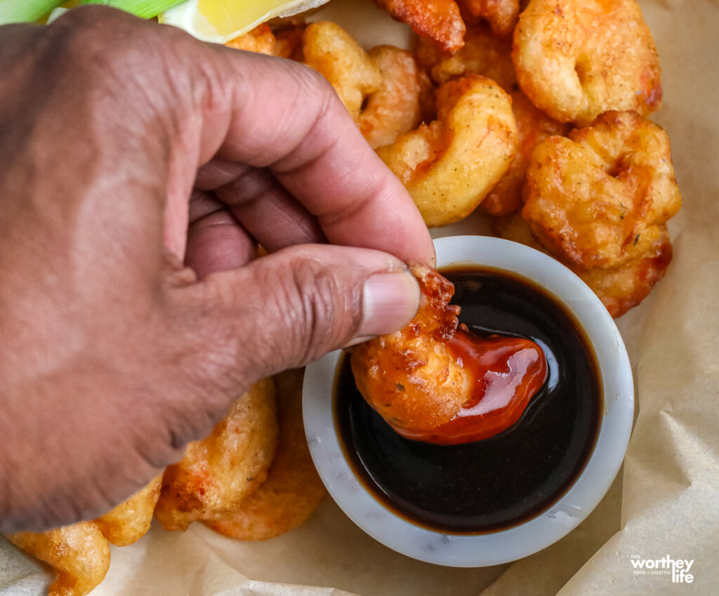 man's hand dipping shrimp into dipping sauce
