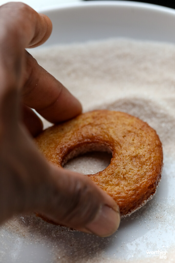 man dipping donut in a sugar cinnamon mix