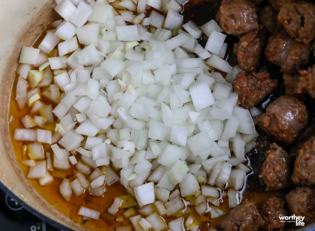 adding onions to a dutch oven with sausage