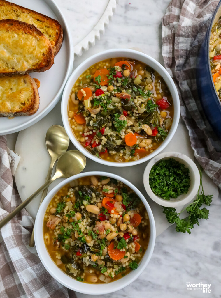 two bowls of Couscous Chickpea Cannellini Bean Soup in white bowls with a side of toasted bread