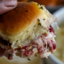 a man holding a turkey and cranberry slider with cheese