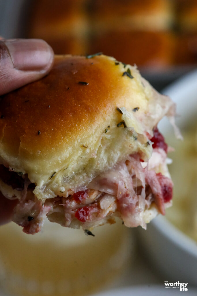 a man holding a turkey and cranberry slider with cheese